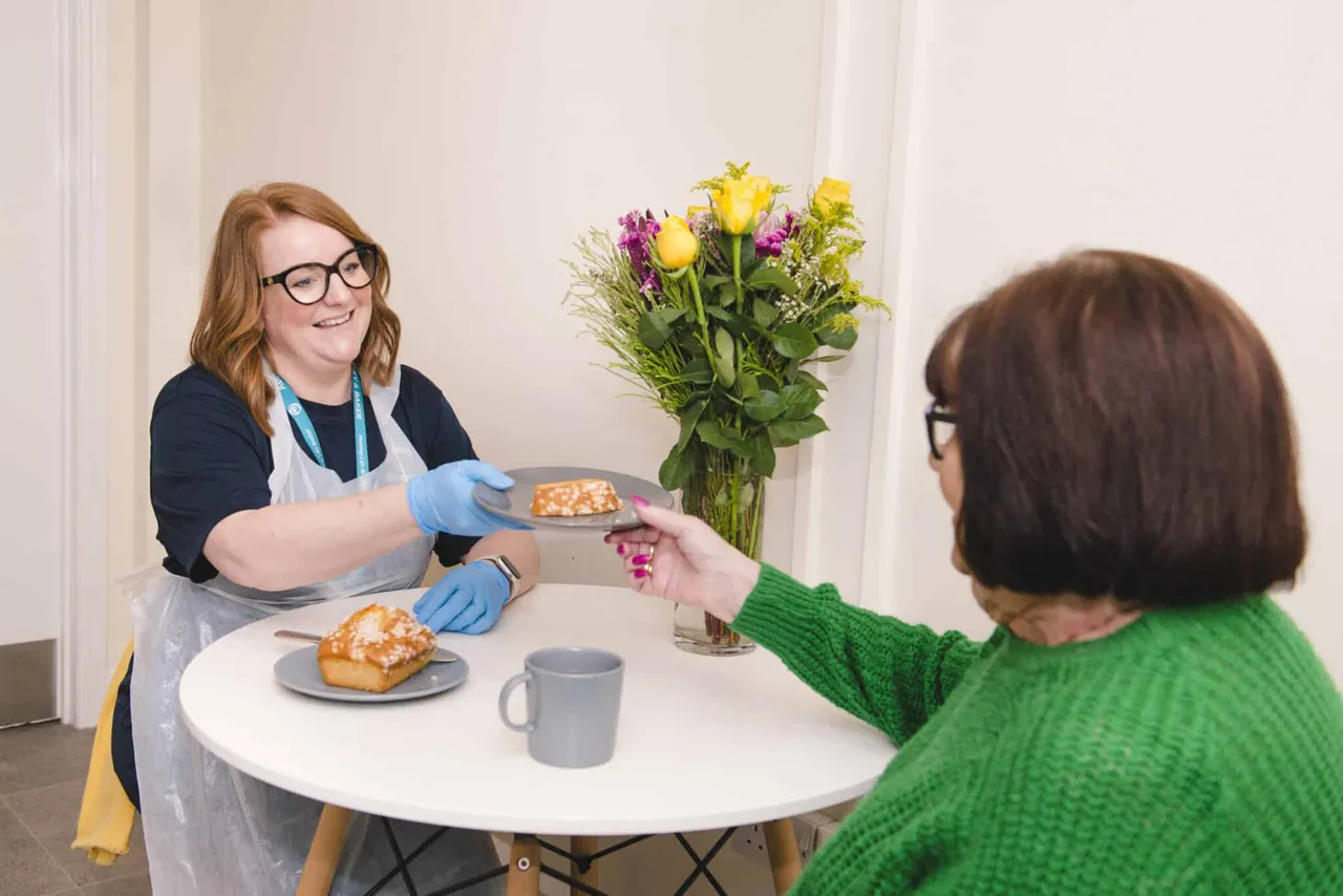 An Abney & Baker carer serving cake to a client during a friendly visit at her table